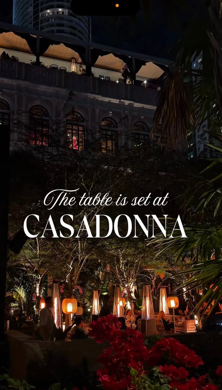 Vue nocturne de la terrasse-jardin illuminée de Casadonna avec le texte « The table is set at Casadonna »